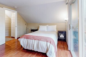 Ein Schlafzimmer mit einem Bett, einem Nachttisch, einem Fenster und einer Tür zu einem anderen Raum.