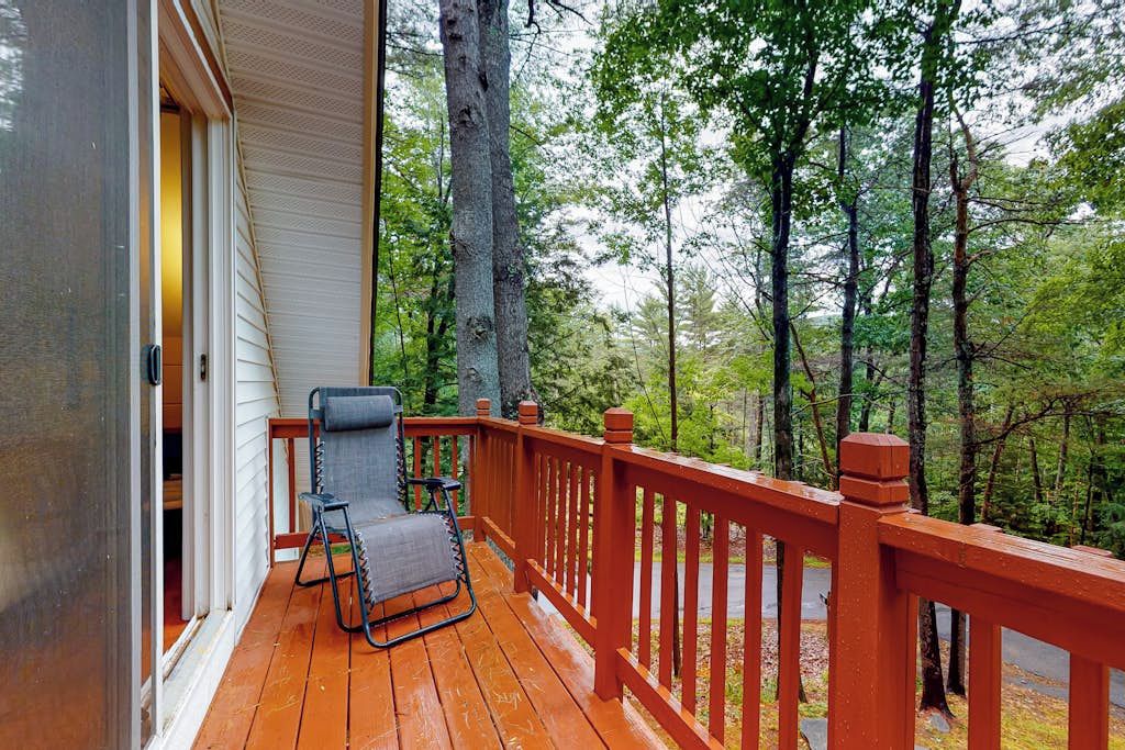 A wooden deck with a red railing, a folding chair, and a view of a forest.