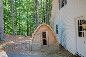 Eine Holzhütte mit einer Tür, umgeben von Bäumen, neben einem Haus mit weißem Verputz.
