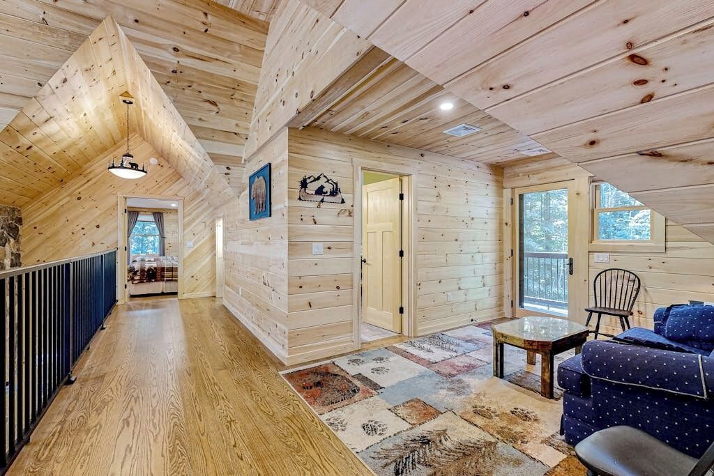 Een houten interieur met een schuine kap, een zithoek met een bank en een stoel, en een kleine tafel.