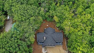 Une maison entourée d’une forêt dense, avec une longue allée et un garage.
