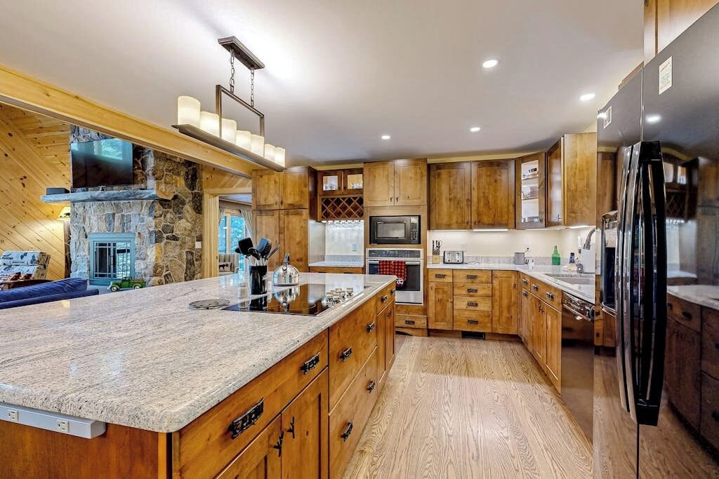 A modern kitchen with wooden cabinets, granite countertops, a built-in oven, and a refrigerator.