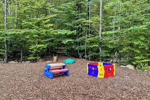 Un parque infantil con tobogán y estructuras para escalar en un área boscosa.