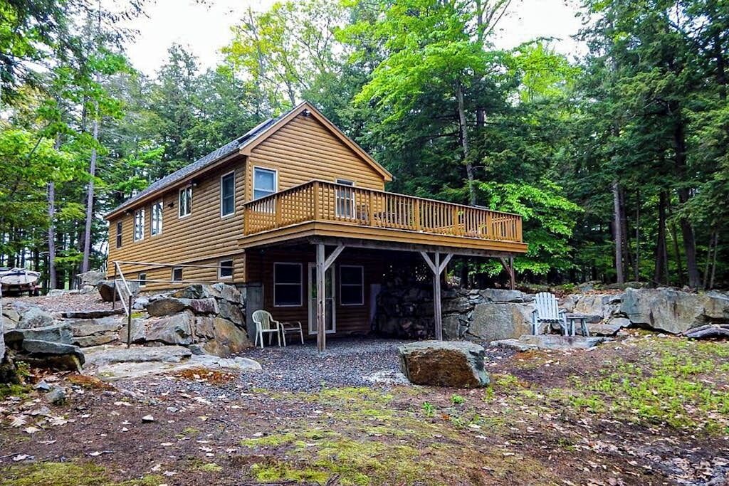 Une cabane en rondins dotée d’un balcon, entourée de rochers et d’arbres.