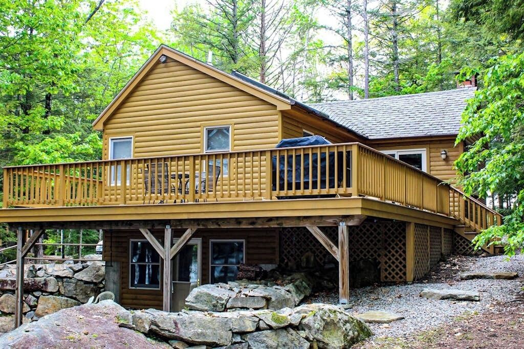 A wooden cabin with a deck, surrounded by trees.