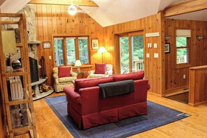 Ein gemütliches Blockhaus-Interieur mit einem roten Sofa, einem Kamin und gro ßen Fenstern.