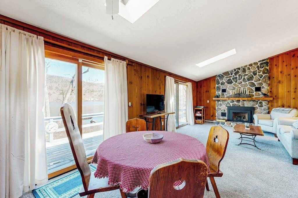 Uma sala de estar aconchegante com lareira de pedra, paredes de madeira, televisão e mesa de jantar com cadeiras.
