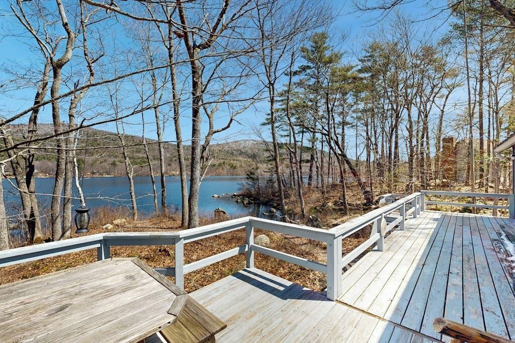 Eine Holzterrasse mit Geländern, mit Blick auf einen See und Bäume.