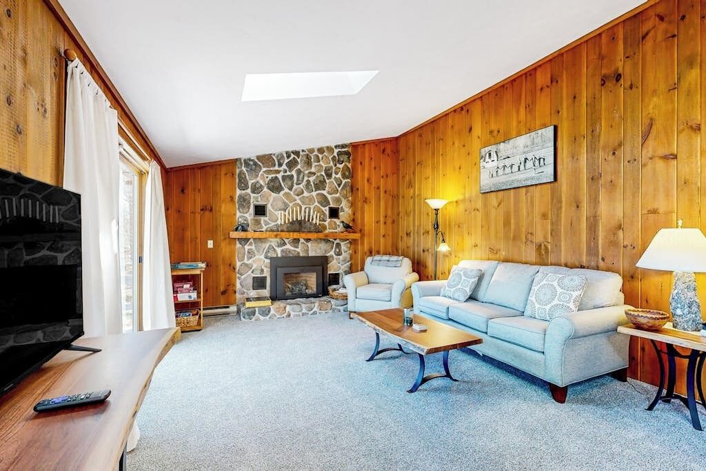 A living room with a stone fireplace, wooden walls, a sofa, and a television.