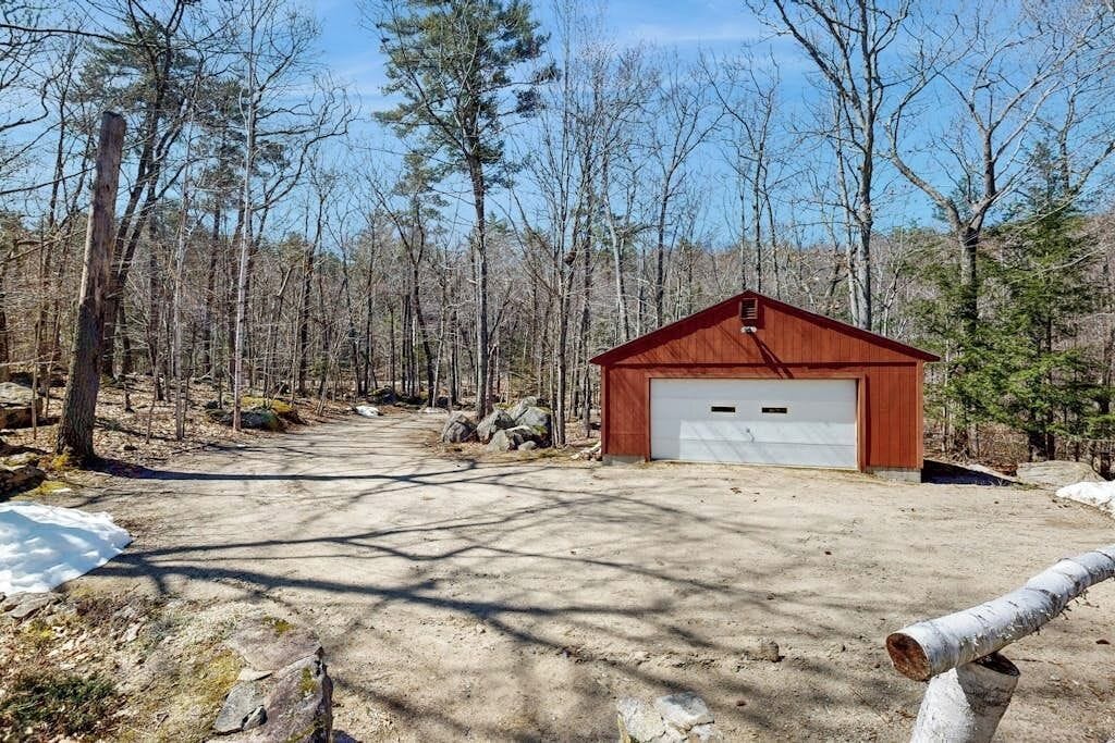 A single-story building with a garage, surrounded by a forested area with a dirt path leading to it.