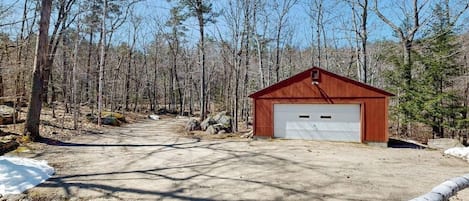 A single-story building with a garage, surrounded by a forested area with a dirt path leading to it.