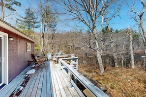 Eine Holzterrasse mit Sitzgelegenheiten, mit Blick auf ein bewaldetes Gebiet.
