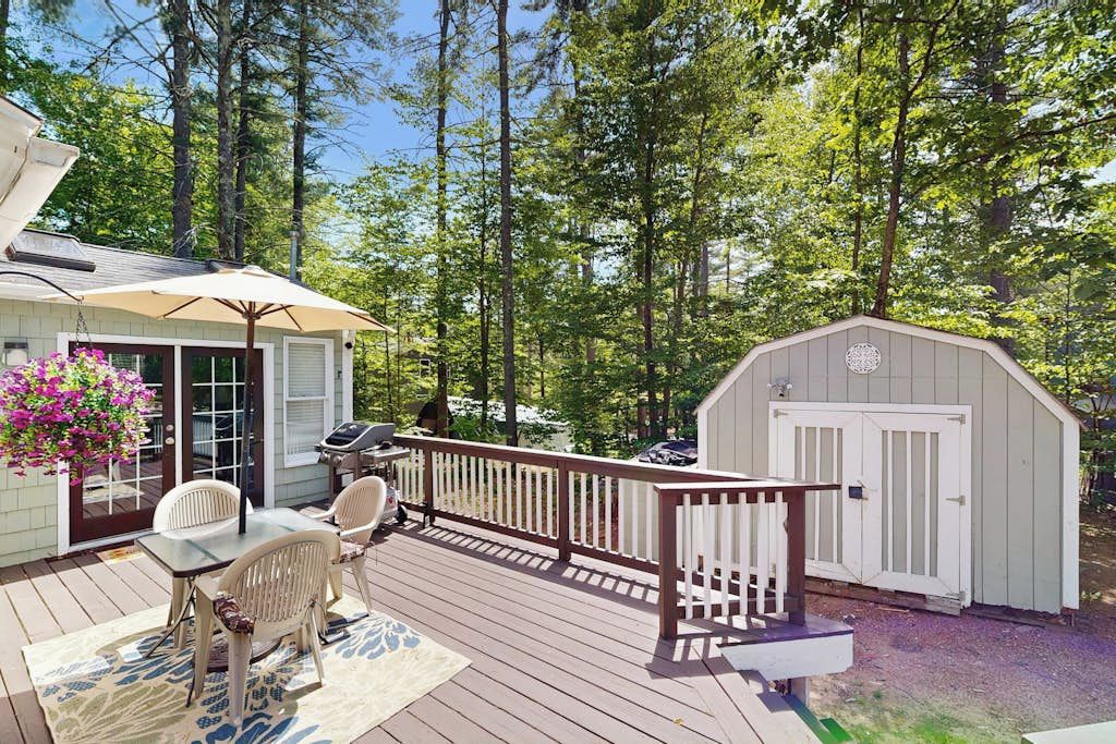 Une terrasse avec une table et des chaises, un barbecue et un abri de jardin, le tout situé dans un espace boisé.