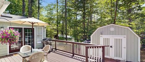 Une terrasse avec une table et des chaises, un barbecue et un abri de jardin, le tout situé dans un espace boisé.