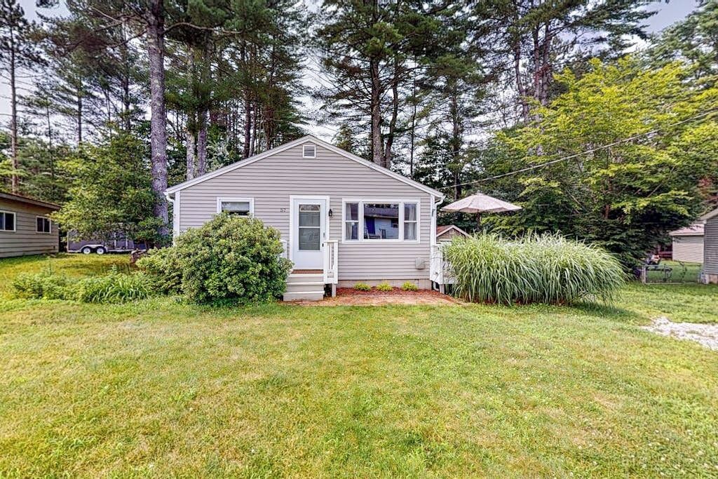 A single-story house with a front porch, surrounded by a well-maintained lawn and dense trees.