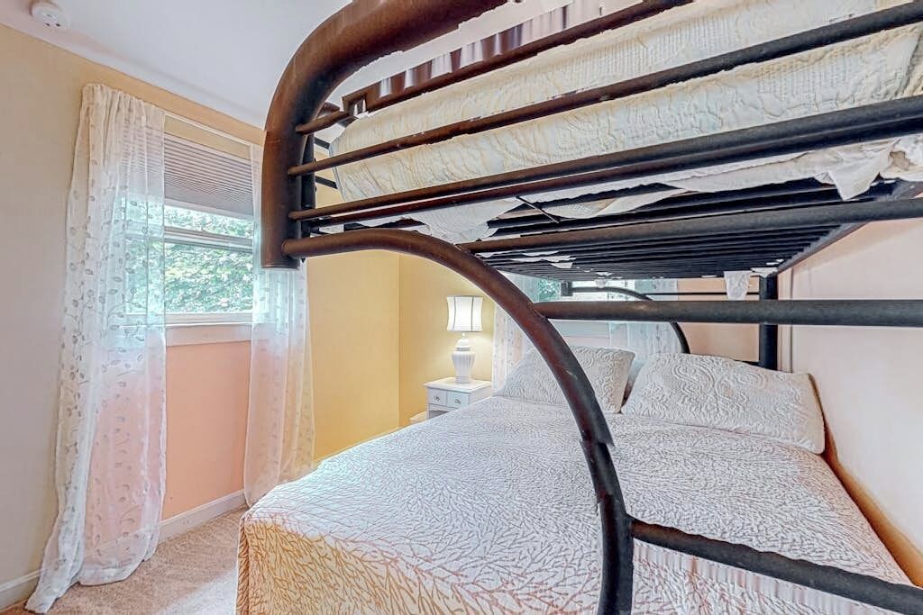 Un lit superposé avec une tête de lit, une fenêtre avec des rideaux et une table de chevet avec une lampe.