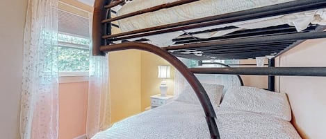 Un lit superposé avec une tête de lit, une fenêtre avec des rideaux et une table de chevet avec une lampe.