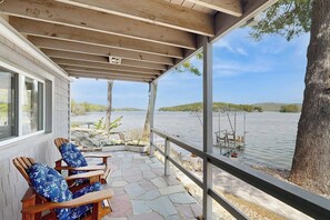 Un espace extérieur abrité, doté d’un sol en pierre, de chaises en bois et offrant une vue sur un lac.
