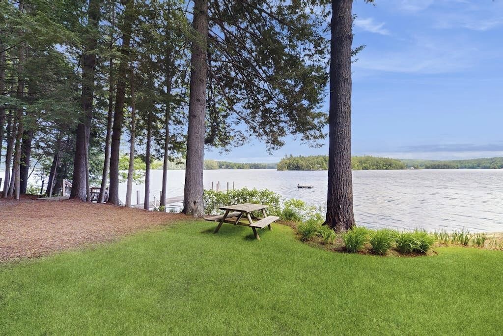 A picnic table in a grassy area with trees and a lake in the background.