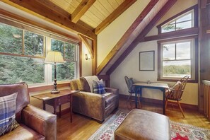 A cozy room with a leather sofa, a small table, and a chair. There are large windows with a view of trees. - 3BR lakefront home: pvt beach, dock, gazebo (Center Harbor)