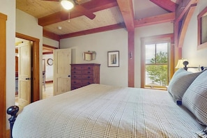 Een slaapkamer met een groot bed, houten balken in het plafond, een dressoir en een raam met uitzicht.