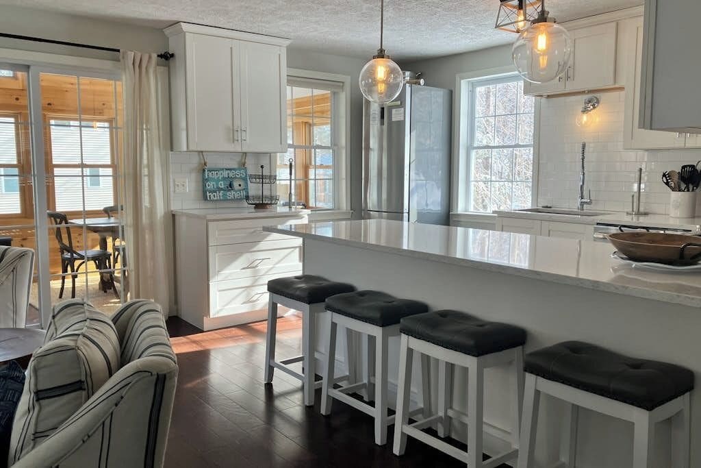 A modern kitchen with white cabinetry, a central island with stools, and pendant lighting.