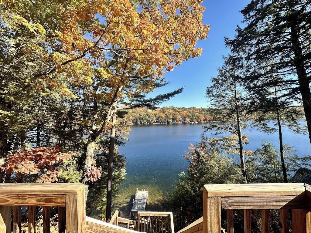 A wooden deck overlooking a lake surrounded by trees with autumn foliage.