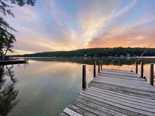 Un muelle de madera se adentra en aguas tranquilas con un atardecer al fondo.