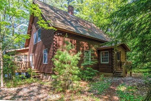 A log cabin with a porch, surrounded by dense forest. - Charming 3BR Lakefront - Dock - Deck (Center Harbor)