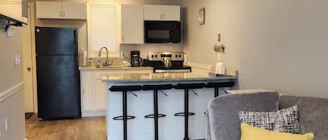 A kitchen with a refrigerator, microwave, stove, and bar stools.