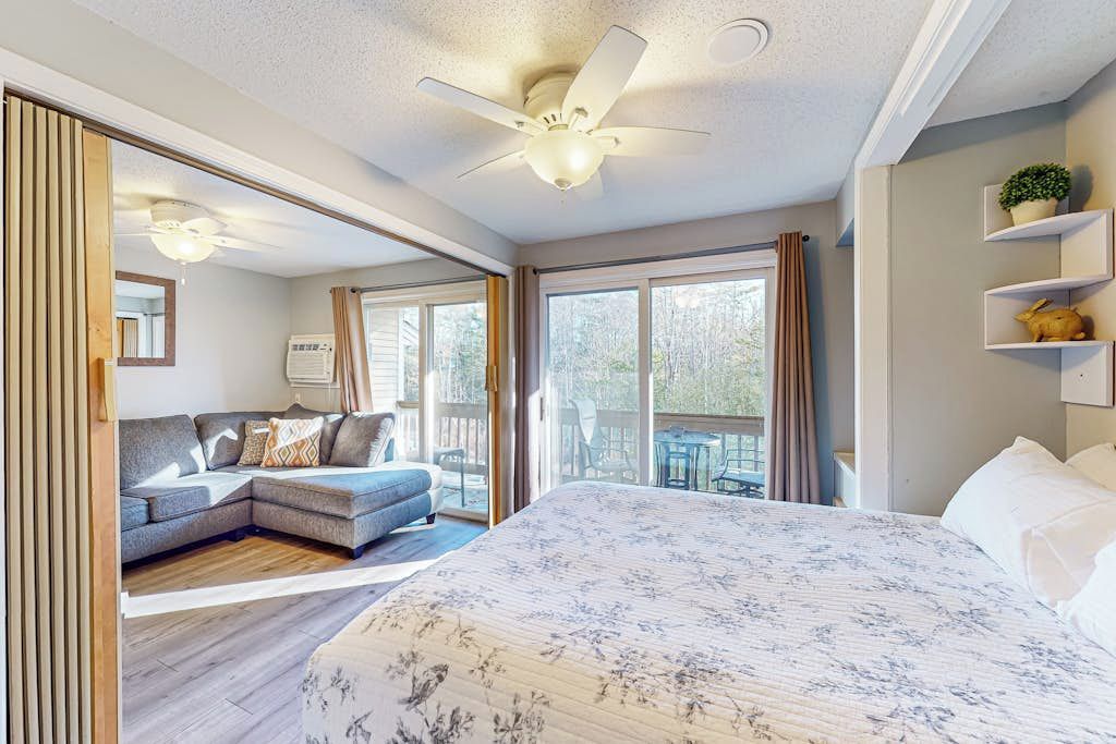 Een slaapkamer met een groot bed, een bank, een plafondventilator en uitzicht op het omliggende landschap.