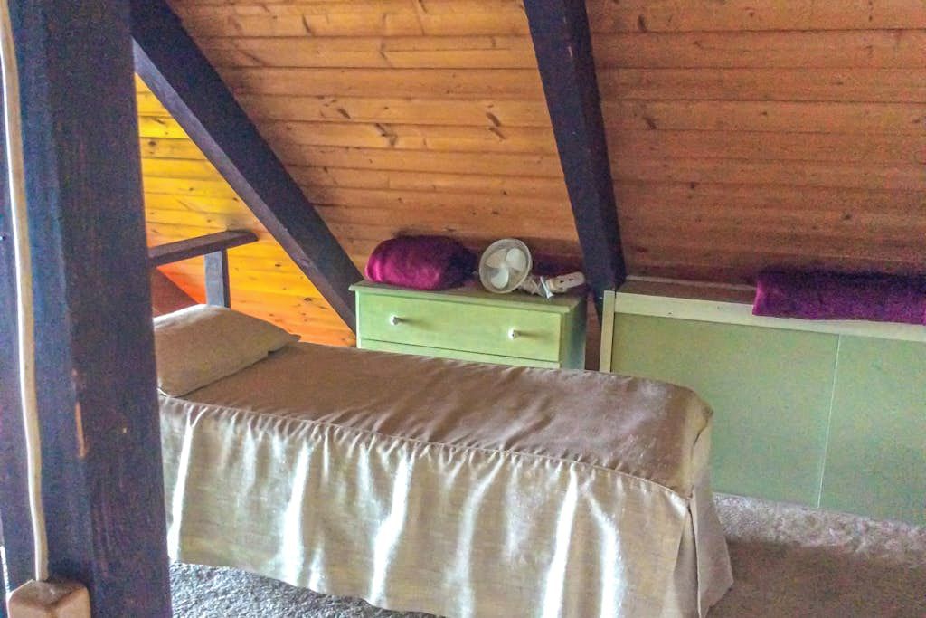 Une petite chambre avec un lit simple, un plafond en bois et une table de chevet verte.