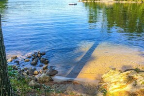 A calm lake with clear water, rocks, and a tree on the shore. - Lakefront 1BR chalet with dock & amazing view (Meredith)