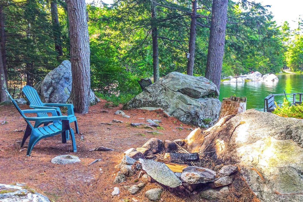 Ein Campingplatz mit Feuerstelle, zwei Stühlen und Blick auf einen See.
