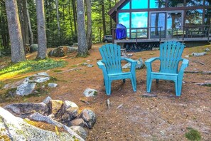 Two Adirondack chairs in a forested area with a cabin in the background. - Lakefront 1BR chalet with dock & amazing view (Meredith)