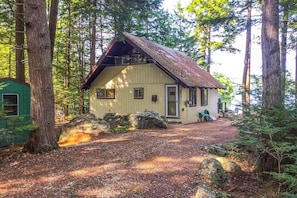A rustic cabin with a sloped roof, surrounded by tall trees and a gravel driveway. - Lakefront 1BR chalet with dock & amazing view (Meredith)