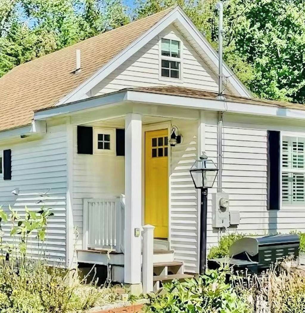 Une maison de plain-pied avec un porche à l’avant, une porte jaune et un petit jardin.