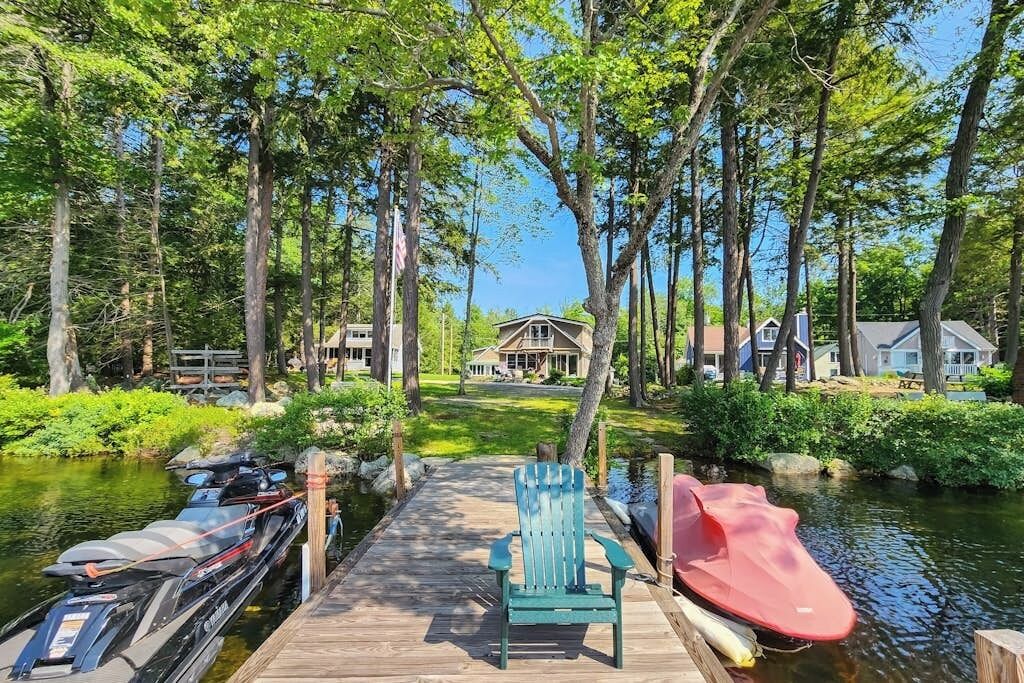 Un quai avec un canot et un jet ski, entouré d’arbres et avec une maison en arrière-plan.