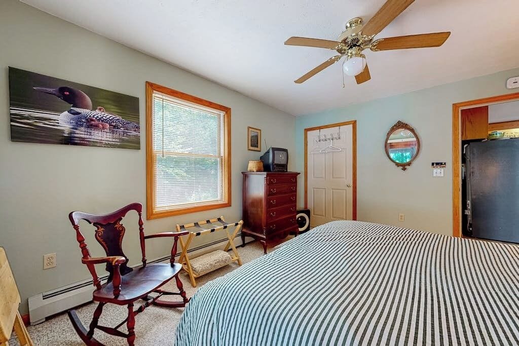Une chambre à coucher comprenant un lit, un fauteuil à bascule, une commode, un téléviseur et un ventilateur de plafond.