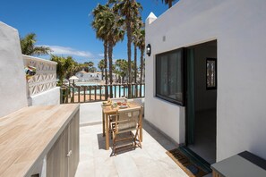 A patio with a table and chairs, a pool in the background, and a view of palm trees. - Corralejo Oasis Duna Casa 3P Adults-Only (Corralejo)