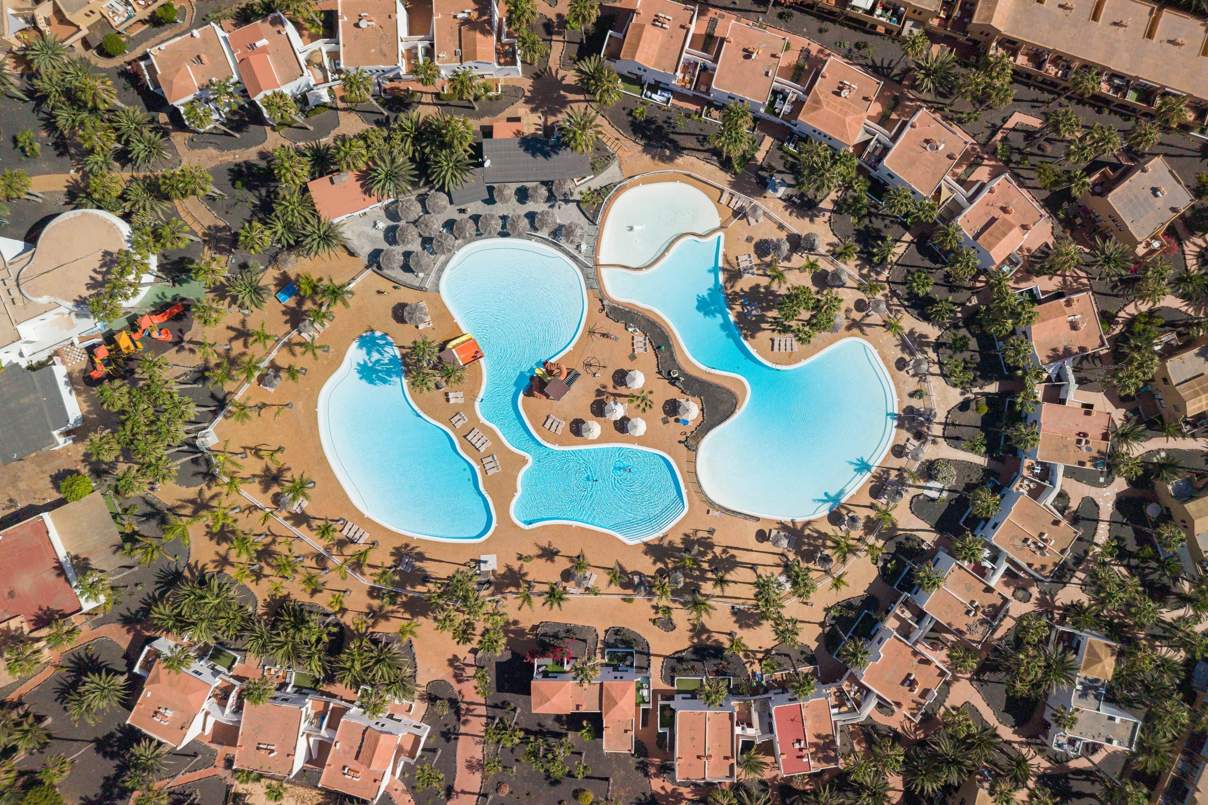 An aerial view of a resort with multiple swimming pools, palm trees, and resort buildings.