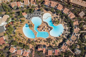 Ett flygbildsbild av ett semesterområde med flera pooler, palmer och byggnader som tillhör området.