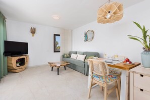 Ein modernes Wohnzimmer mit Flachbildfernseher, Couch, Couchtisch und einer Essecke für zwei Personen.