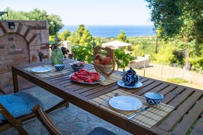 An outdoor dining table with a view of the sea, a vase with flowers, a bowl of fruit, and a teapot. - Halkidiki Kassandra villa 3P Peace & Beautiful Sea (Agia Paraskevi)