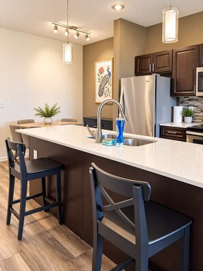 A modern kitchen with a central island, stainless steel appliances, and bar stools.