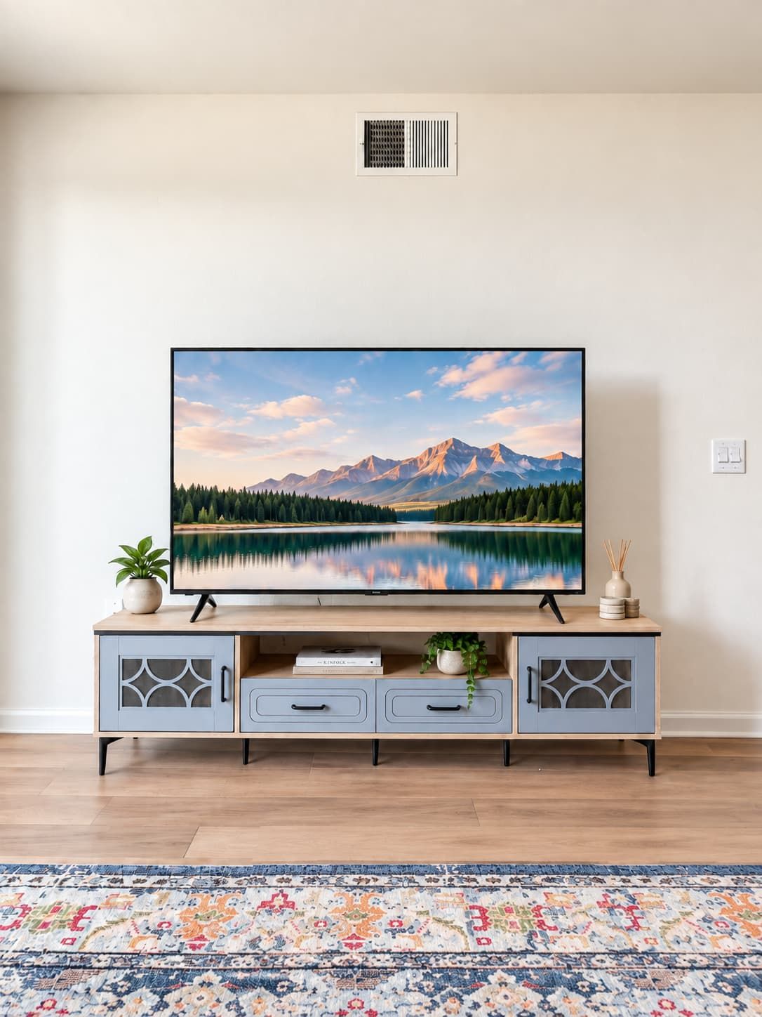 Un téléviseur à écran plat posé sur un meuble télé en bois, avec un papier peint représentant un paysage de montagne, une plante en pot et un vase décoratif.