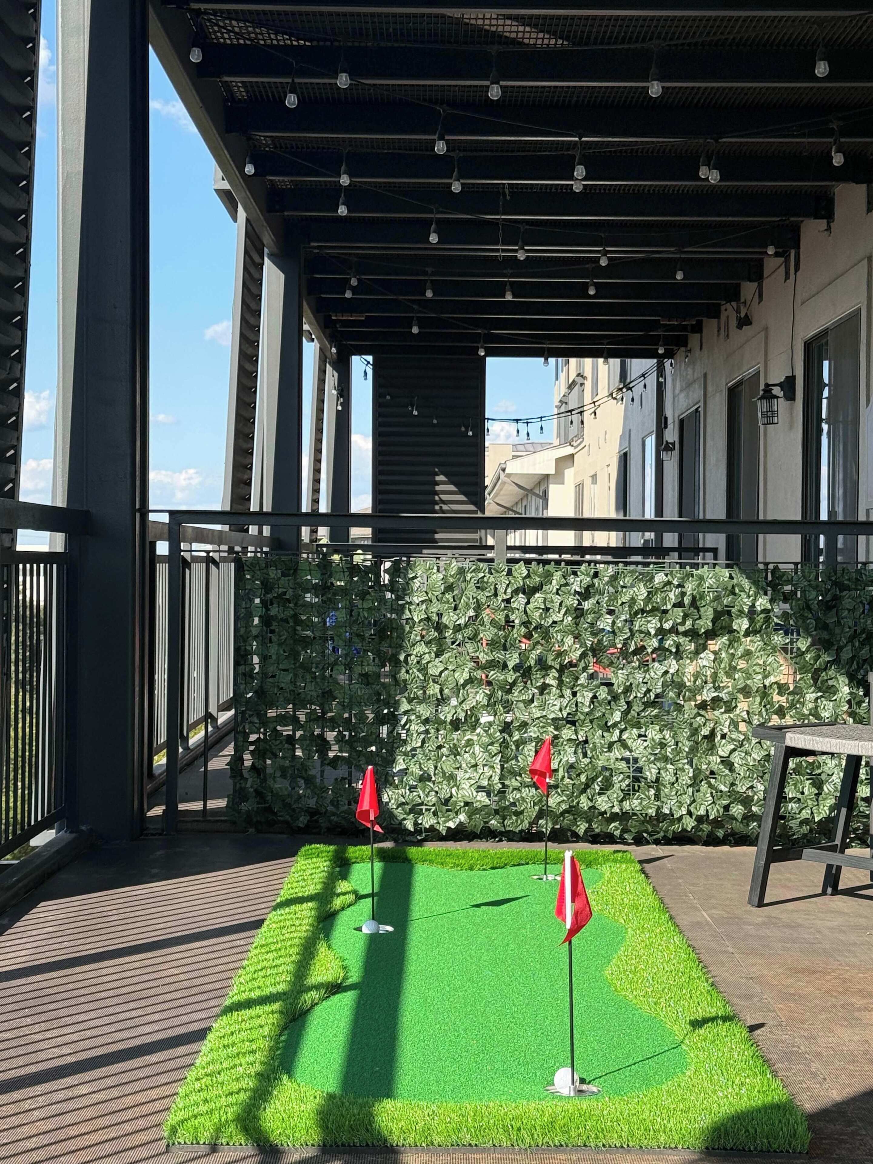 An outdoor area with a green artificial turf, a metal railing, and a wall covered with ivy.