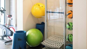 Un gimnasio con equipo de ejercicio, una pelota de estabilidad y un estante de pared con balones deportivos.