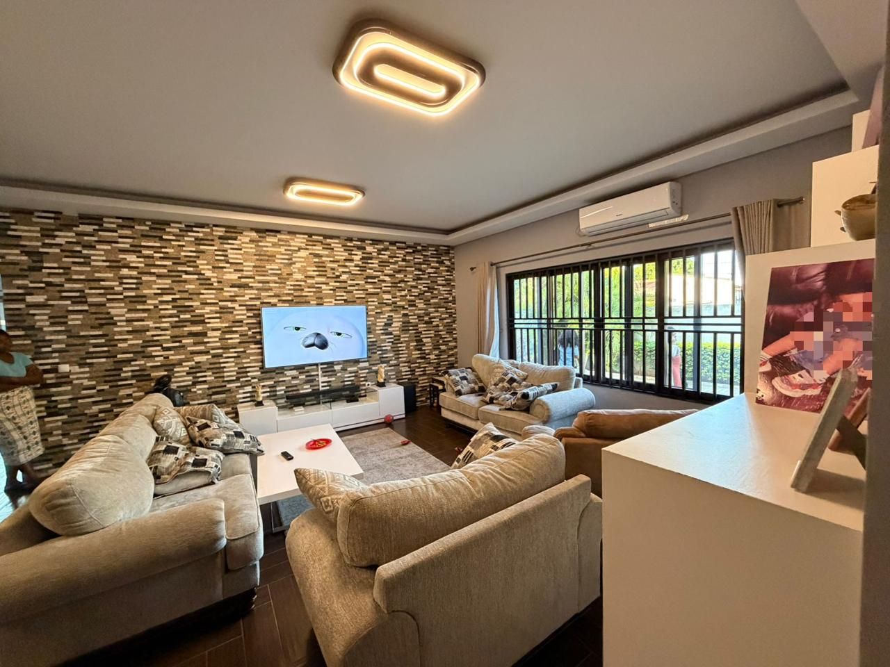 A modern living room with a flat-screen TV, sofas, a coffee table, and a patterned wall.