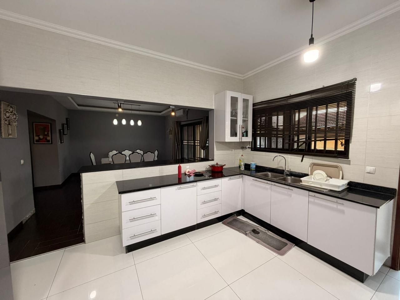 A modern kitchen with white cabinets, a black countertop, and a window with blinds.